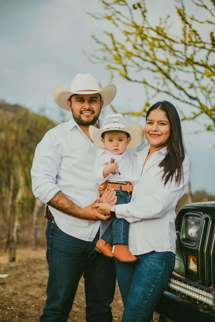 A family of three enjoying a sunny day outdoors, all wearing white shirts and cowboy hats.